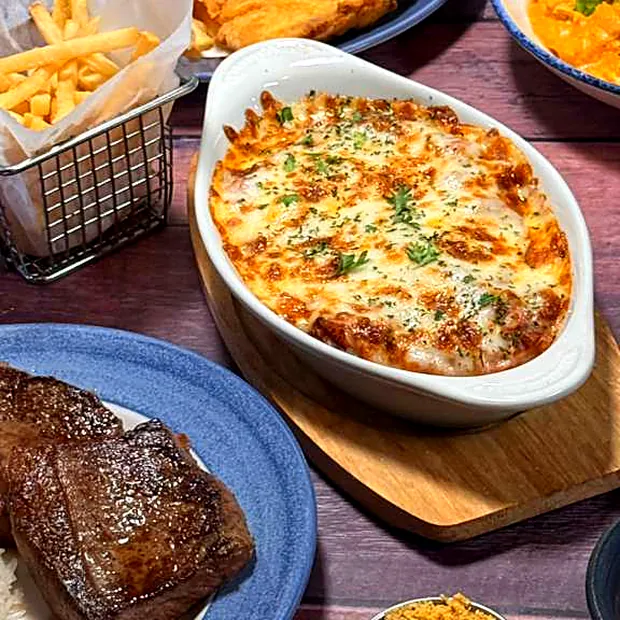 Mesa servida no restaurante Sabor Brasil com carne na chapa, gratinado, porção de fritas e farofa